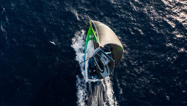 Aerial view of a sailboat with green and black sails cutting through dark ocean water.