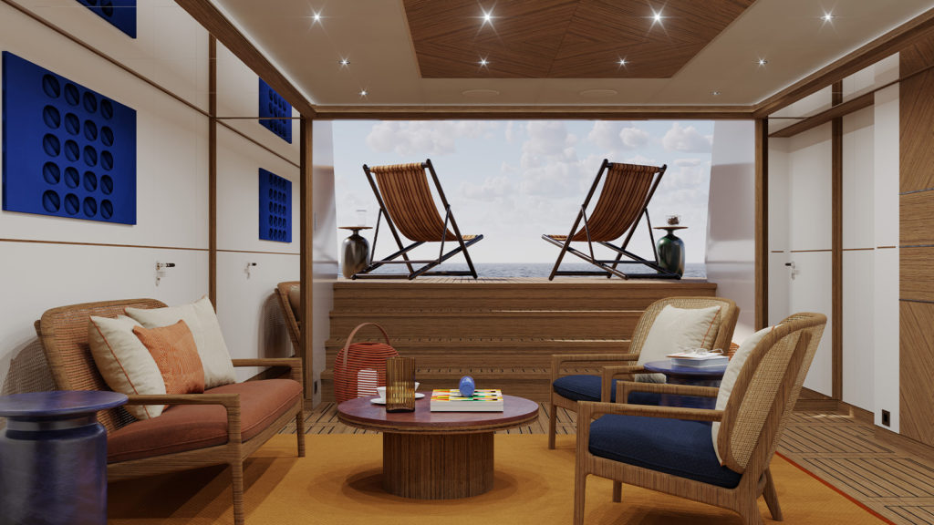 A luxurious interior with wooden accents featuring two cushioned lounge chairs, a small round table, and a board game set on an orange carpet. Glass doors open to a deck with two wooden deck chairs facing the ocean under a partly cloudy sky.