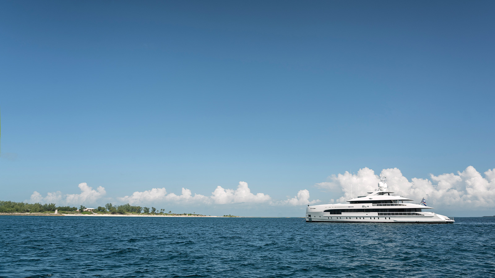 A luxury yacht sailing on a calm sea with a clear blue sky and distant island visible in the background.